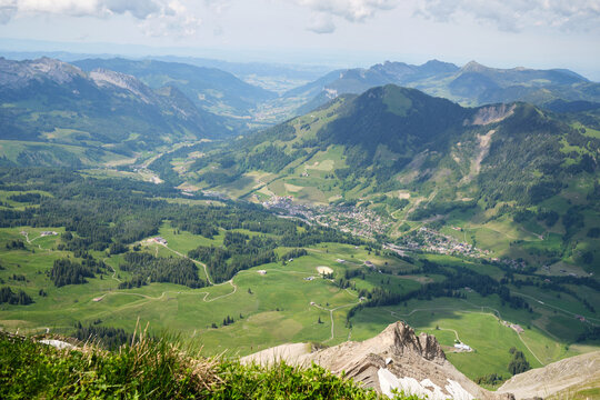 A panoramic view of the green valleys and mountains of Brienz, Switzerland, showcasing lush meadows and dense forests under a partially cloudy sky.