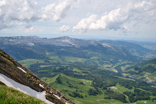 Panoramic view of lush green valleys and mountains in Switzerland, showcasing Brienz's stunning natural beauty. Snow-capped peaks and rolling hills create a serene landscape.