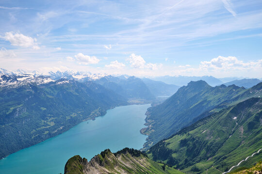 Stunning aerial view of Lake Brienz surrounded by majestic mountains in Switzerland, showcasing vibrant green meadows and snow-capped peaks beneath a blue sky.