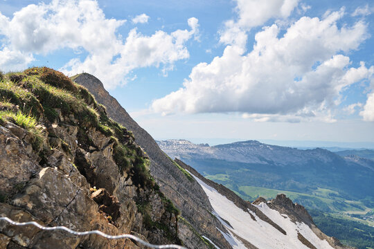 Majestic mountains in Switzerland, near Brienz, showcase rocky cliffs and vibrant greenery, with patches of snow glistening under the blue sky and wispy clouds.