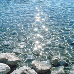 Fototapeta premium Clear water with sparkling reflections and smooth stones along shore