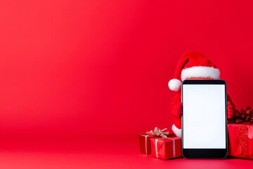 Claus's Smartphone Christmas Surprise - Festive Christmas scene: Santa hat on a smartphone with blank screen, beside red gifts. Symbolizing online shopping, holiday cheer, technology, gifting, and win