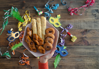 Woman hands in red sweater with plate of carnival sweets. Wooden background with carnival...