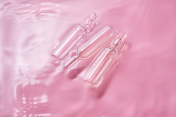 Ampoules in water on a pink background.