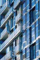 Fototapeta premium Tall, modern high rise building featuring glass windows and metallic balconies. Blue shades dominate the color palette.