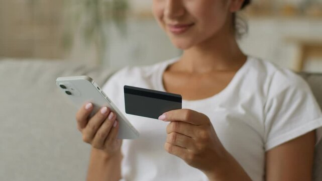 Happy smiling carefree Indian woman Arabian female girl buyer client enter secure number of credit bank card banking online mobile phone shopping smartphone distant purchase buy pay internet at home