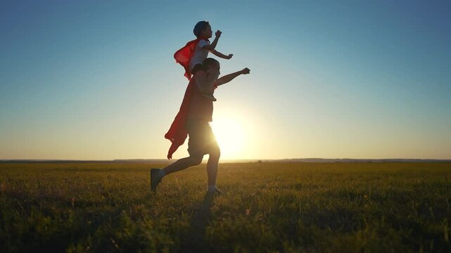 Father and son running superhero silhouette. Child family super concept. Silhouette of a superhero with his daddy and baby. Silhouette of superhero with father and son running grass on.