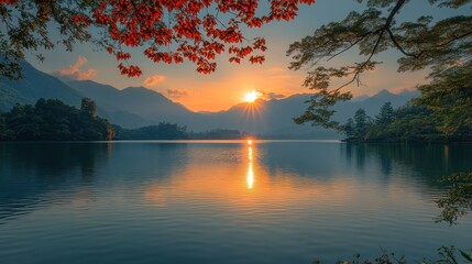 Serene sunrise over calm lake with mountain backdrop and autumn leaves.