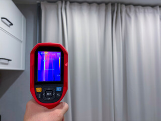 Technician uses thermal imaging camera to identify heat loss from window, exposing temperature...
