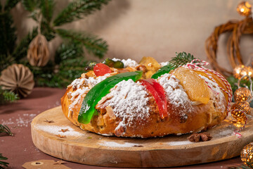 Colorful candied fruits and powdered sugar on a traditional Bolo Rei or Kings Cake, set on a wooden board amidst warm holiday decorations and lights. Is tradicional for Christmas in Portugal.