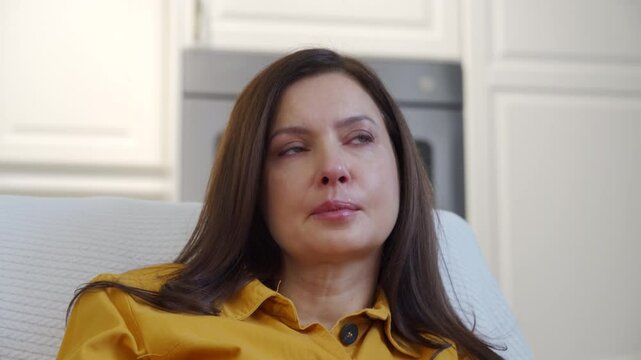 Emotional woman sitting on sofa in living room in front of TV watching melodrama. Impressionable woman cries wiping tears worried while watching movie.