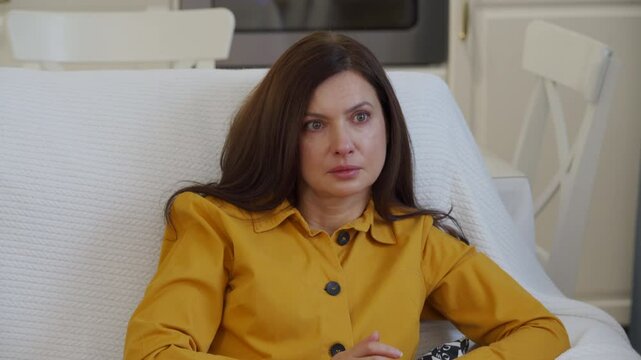 Impressionable woman sitting on sofa in living room in front of TV watching melodrama. Tear stained face of worried woman while watching movie.