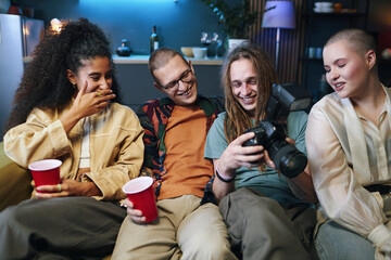 Guy showing his photos to friends while they sitting on sofa during party