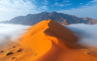 Majestic orange sand dune in a desert landscape with mountains and fog.