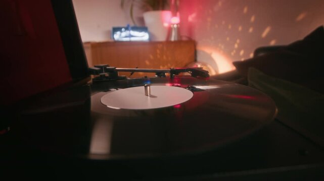Closeup low key shot of hand of faceless lady putting down needle on phonograph record while playing music on vinyl record player indoors