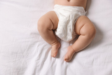 Cute little baby in diaper on bed, top view