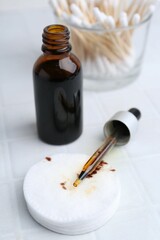 Bottle of iodine with dropper, cotton pads and swabs on white tiled table, closeup