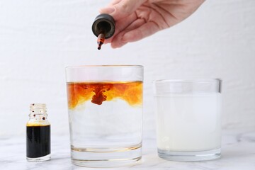 Iodine starch test. Woman dripping aqueous iodine into glass of water at white marble table, closeup