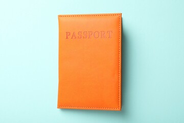 Passport in orange cover on light blue background, top view