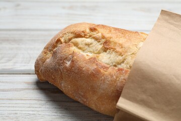 Paper bag with fresh baguette on wooden table, closeup