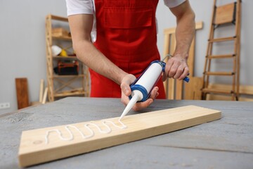 Worker with caulking gun glueing wooden plank indoors, closeup