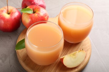 Tasty apple juice in glasses and fresh fruits on grey table, closeup