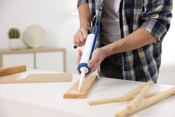 Man with caulking gun glueing wooden plank indoors, closeup