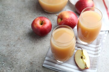 Refreshing apple juice in glasses and fruits on grey textured table. Space for text