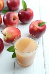 Refreshing apple juice in glass and fruits on white wooden table