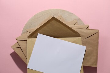 Kraft paper envelopes and letter on pink background, top view. Mockup for design