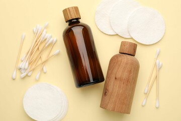 Cotton pads, bottles of cosmetic products and swabs on beige background, flat lay