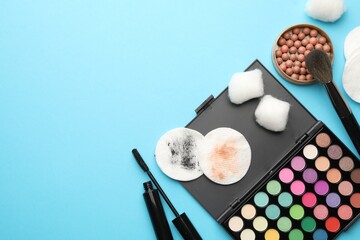 Flat lay composition with cotton pads and makeup products on light blue background, space for text