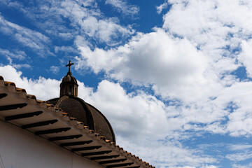 Roof of a church with the cross clearly visible against a backdrop of a blue sky filled with clouds.