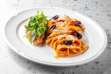 Delicious pasta served on a white plate, garnished with olives and grated cheese, accompanied by a side of fresh salad. A vibrant and appetizing dish ideal for food photography.