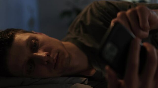 Man scrolling through phone in bed at night, struggling with sleeplessness and overstimulation from digital content.