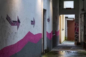 Fotobehang Gang Urban Alleyway with Abstract Arrow Wall Art. Graffiti-Adorned Passage Leading to a Courtyard. Pärnu. Estonia. 27.12.2024.  © Edijs