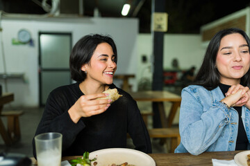 Two joyful women savoring authentic mexican cuisine, bonding over a meal and chat in a lively taqueria