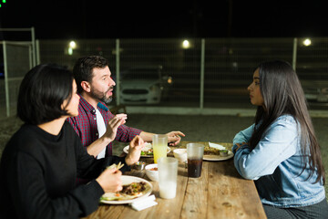 Group of friends having a lively conversation over tacos and drinks at a taqueria in the evening
