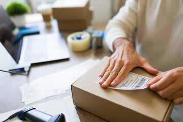 Small business owner applying shipping label to cardboard box, preparing packages for delivery in a...