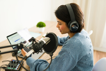 Content creator speaking into a microphone and recording audio podcast at home studio using...