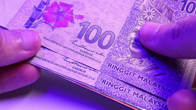 Man's hands counting brand new Malaysian ringgit (MYR) under the flashing light of a police siren. Close up view. Selective focus. Concept of financial crime in Malaysia.