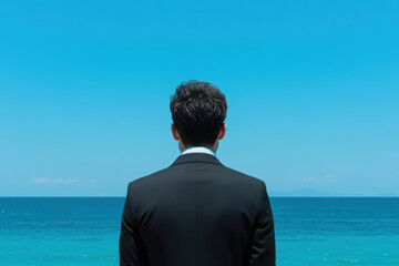 Fototapeta premium 海辺で背を向ける男性が晴れた空と青い海を眺める瞬間
