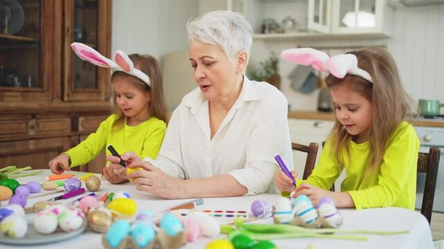 Happy Easter. Two little girls sisters twins grandmother painting eggs enjoying time together. Happy family grandma granddaughters child kids preparing for Easter. Spring Christian festival tradition