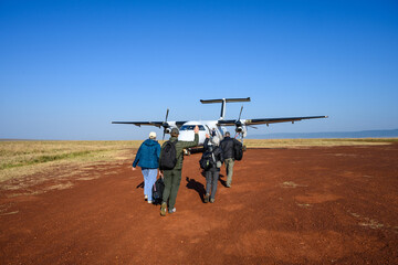 Group of people walking out on dirt airstrip to airplane waiting to take them to next safari camp, African adventure safari in Kenya  © knelson20