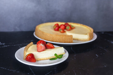 Classic sliced homemade New York cheesecake with fresh strawberries served on a black marble countertop. Homemade dessert.