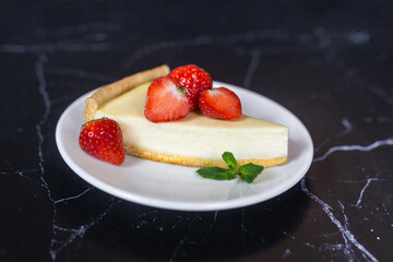Classic sliced homemade New York cheesecake with fresh strawberries served on a black marble countertop. Homemade dessert.