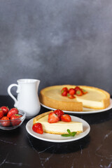 Classic sliced homemade New York cheesecake with fresh strawberries served on a black marble countertop. Homemade dessert.