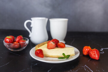 Classic sliced homemade New York cheesecake with fresh strawberries served on a black marble countertop. Homemade dessert.