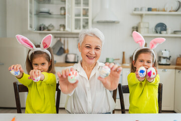 Happy Easter. Two little girls sisters twins grandmother painting eggs enjoying time together. Happy family grandma granddaughters child kids preparing for Easter. Spring Christian festival tradition