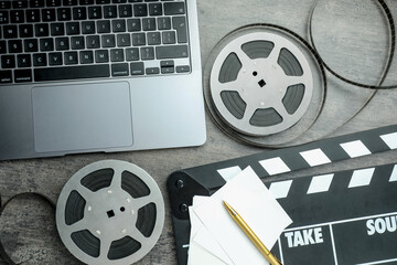 Flat lay composition with movie clapper, film reels and laptop on grey textured table